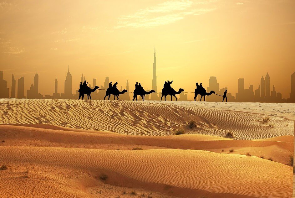 Camel caravan on sand dunes on Arabian desert with Dubai skyline