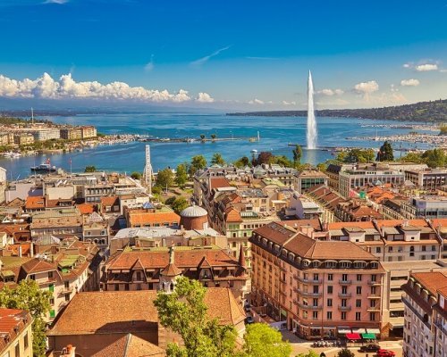 Geneva skyline cityscape, French-Swiss in Switzerland. Aerial view of Jet d'eau fountain, Lake Leman, bay and harbor from the bell tower of Saint-Pierre Cathedral. Sunny day blue sky.